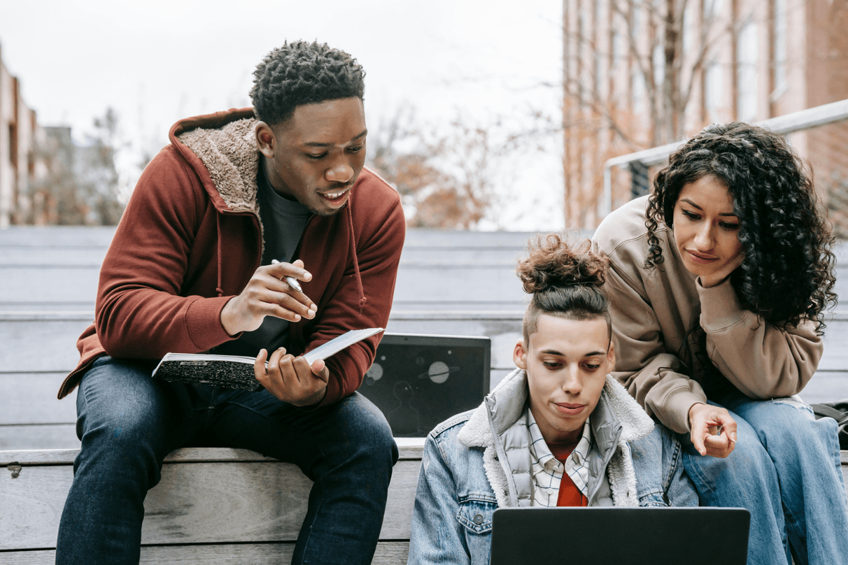 Three students sitting together and looking at a laptop, smiling